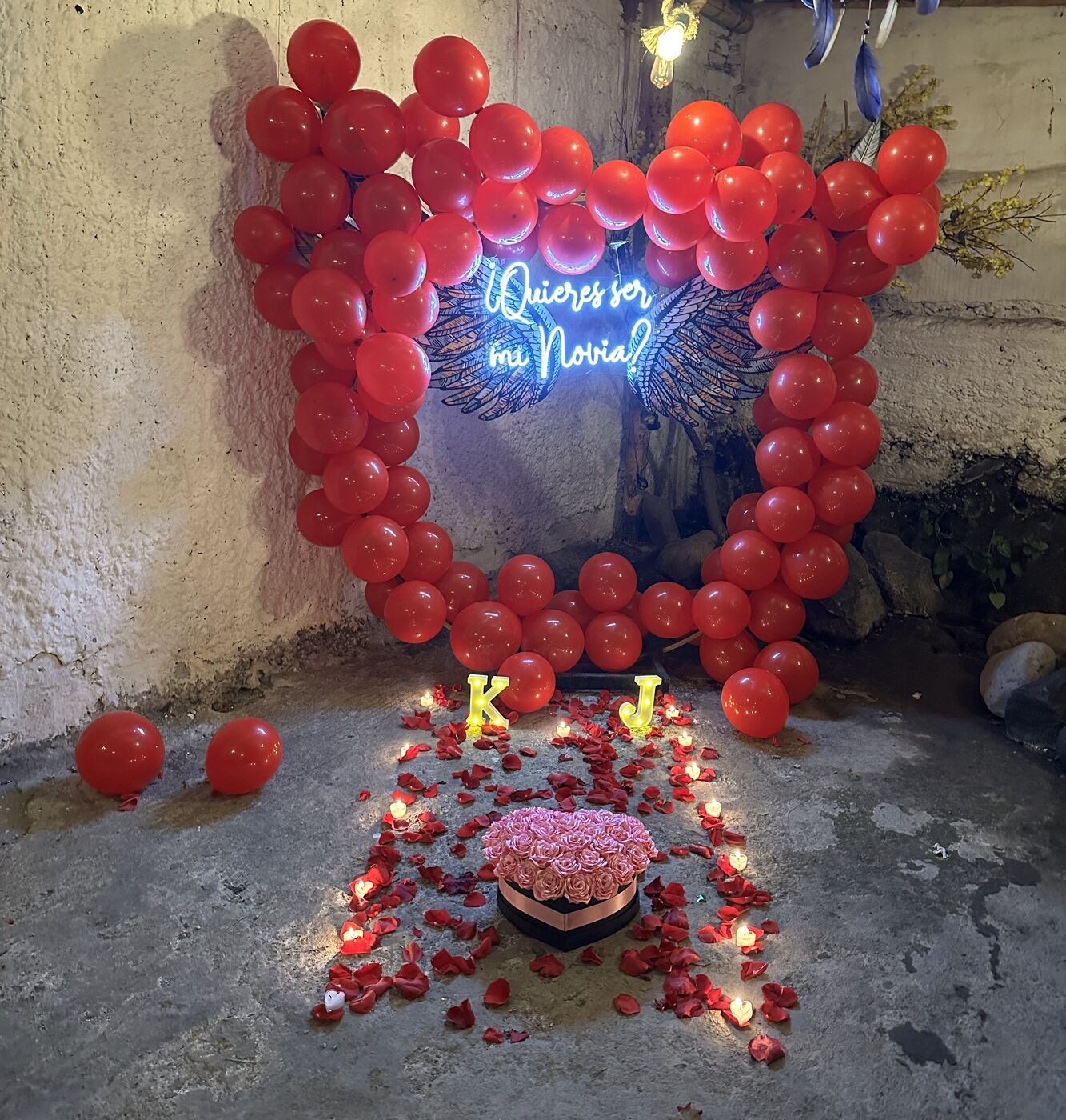 Corazón de globos rojos con letrero de neón Quieres ser mi novia, pétalos y velas